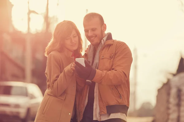 sweet couple using smartphone  while standing on blurred street background