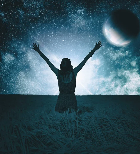 black female silhouette with raised hands standing in meadow against colorful night sky