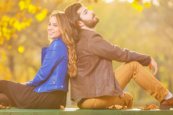 couple in love sitting back to back on wooden bench in autumn forest at sunset