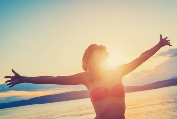 笑みを浮かべて 海岸に立っている上げられた手とサングラスで幸せな魅力的な女性 — ストック写真