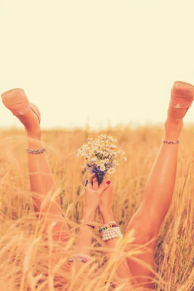 在麦田里躺着花花束的女人抬腿和手 — 图库照片
