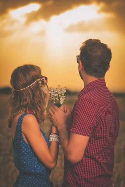 手を繋いでいると 草原に夕日を見て野生の花の花束と幸せな甘いカップル — ストック写真