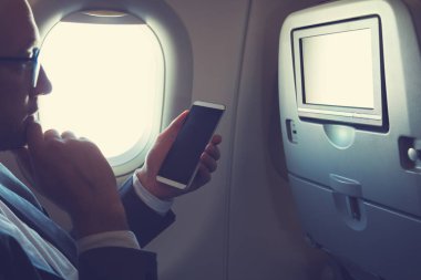 Uçağın içinde Smartphone kullanarak ve düşünce pencereden bakarak adam.
