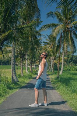 Palmiye ağaçları ile boş bir yolun ortasında duran adam.
