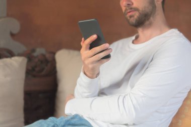 Kanepede oturan ve cep telefonu kullanan adam.