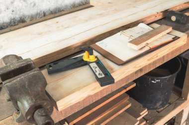 Marangoz araçları, ahşap plakalar, kelepçe, paslı bir tablo üstünde defter.