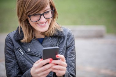 Cep telefonu kullanarak sevimli genç kadın / manifatura açık havada.