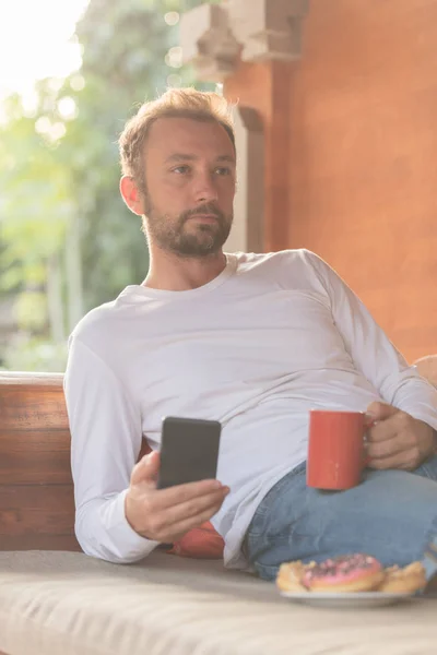 Hombre Sosteniendo Teléfono Celular Taza Café Con Donaciones Sofá — Foto de Stock
