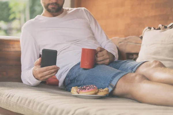 Hombre Sosteniendo Teléfono Celular Taza Café Con Donaciones Sofá — Foto de Stock