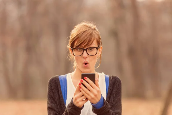 Cute girl reading surprising news on smart-phone.