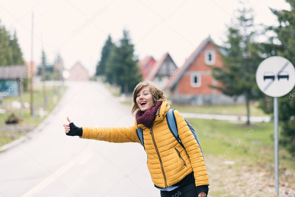 Girl with thumb-up hitchhiking on a suburb road.