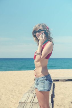 Sahilde cep telefonu kullanan genç kadın.