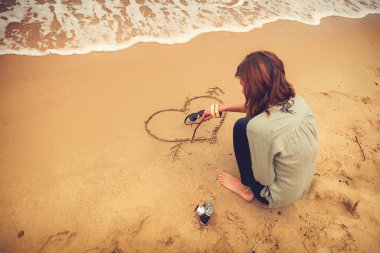 Kız sahilde bir kalp şekli sembolü yapma.