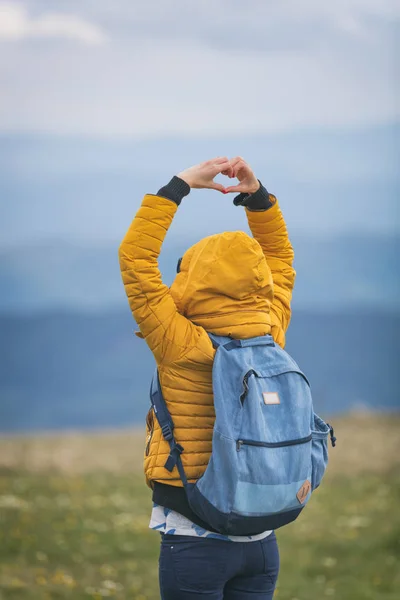 Girl making a heart-shape with mountain landscape in the background.