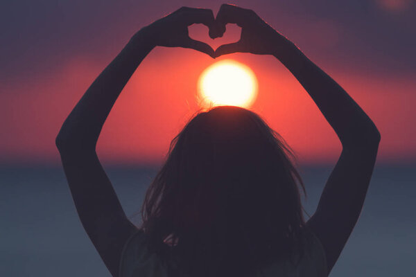 Девочка, держащая форму сердца для заката океана / моря
.