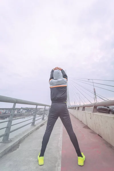Urban jogger stretching on a big bridge.
