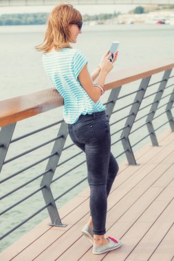 Nehri yakınında iskelede cep telefonu kullanan kız.