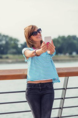 Nehri yakınında iskelede cep telefonu kullanan kız.