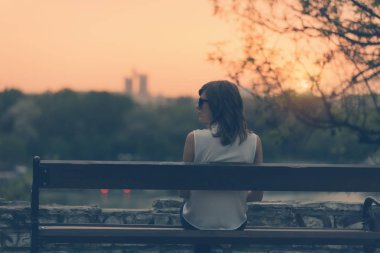 Bir bankta oturan ve uzak şehir manzara izlemek kadın.