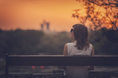 Bir bankta oturan ve uzak şehir manzara izlemek kadın.