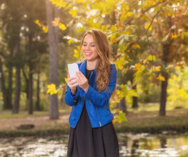 Park Sonbahar ile cep telefonu kullanan genç kız / sonbahar renkleri.