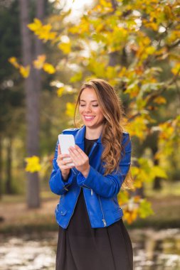Park Sonbahar ile cep telefonu kullanan genç kız / sonbahar renkleri.