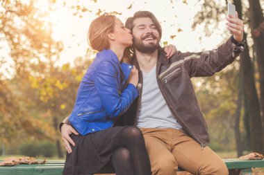 Şirin çift selfie parkta bir bankta sonbahar yapma / sonbahar sezon.