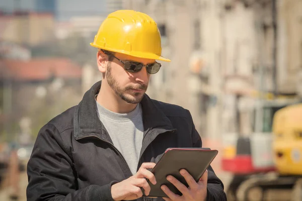 Builder with digital tablet posing on a heavy construction site.