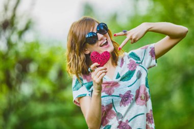 Barış için bir kağıt kalp işareti ve iki parmak - şeklinde - semboller tutan Şirin genç kadın.