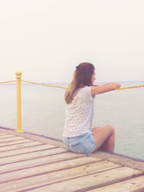 Ahşap bir iskele üzerinde oturan ve okyanusa bakarak kız.