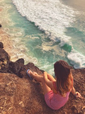 Yalnız kız okyanus üzerinde yüksek bir kayalığın üzerinde oturan.