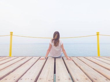Ahşap bir köstebek üzerinde oturan kız / iskele ve okyanusa bakarak.