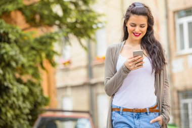 Kentsel ortamda cep telefonu kullanarak sevimli genç kadın.