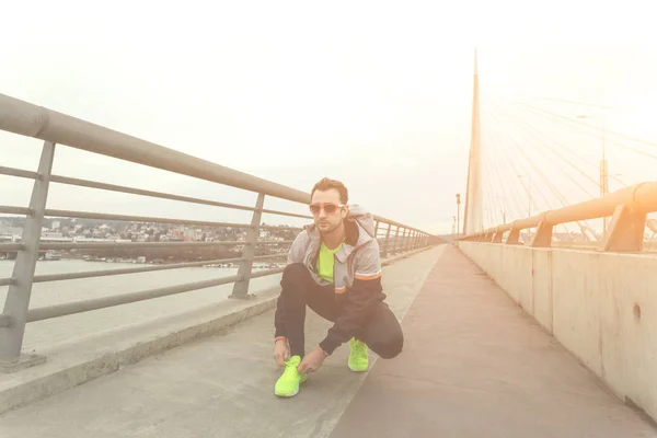 大きな橋の上に靴紐を結ぶ男性ジョガー — ストック写真
