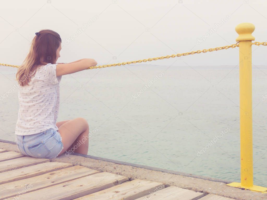 Girl sitting on a wooden pier and looking at the ocean.