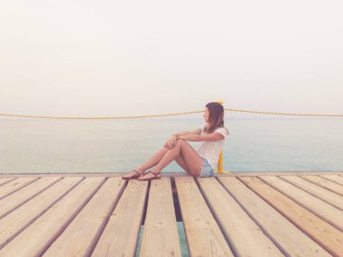 Ahşap bir iskele üzerinde oturan ve okyanusa bakarak kız.