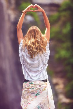 Kalp şekle el ile açık havada tutan kız.