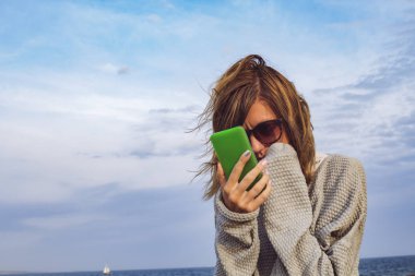 Sevimli kız okyanus kıyısında cep telefonu kullanarak.