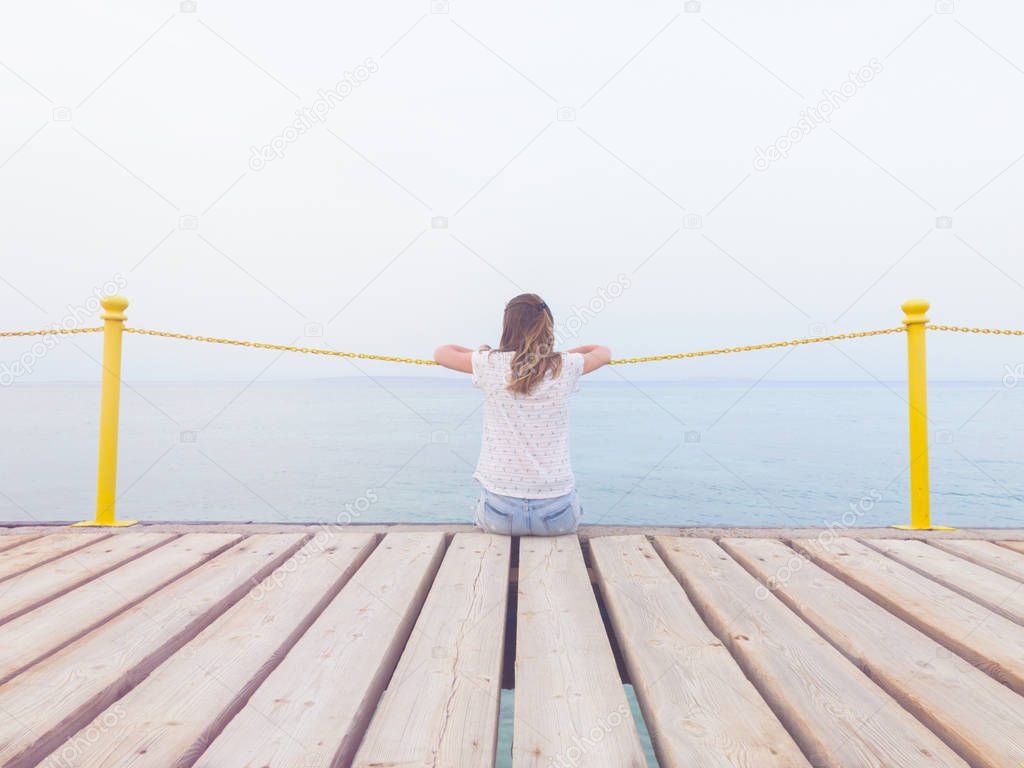 Girl sitting on a wooden mole / pier and looking at the ocean.