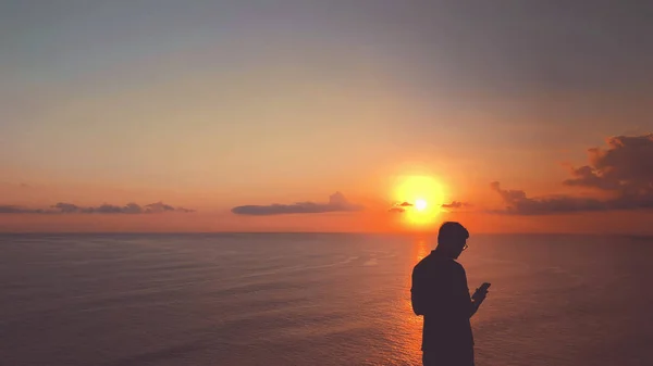 Silhouette of a man with smartphone in sunset time over the ocean.