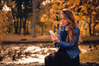 Sevimli kız Park sonbahar renkleri ile cep telefonu kullanarak.