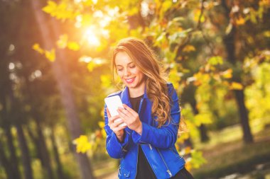 Park sezon sonbahar renkleri ile Smartphone kullanarak sevimli genç kadın.