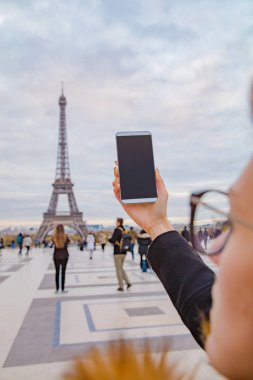 Paris geçmişi ve Eyfel kulesi olan cep telefonu kullanan bir kız..
