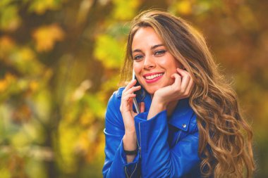 Park sezon sonbahar renkleri ile Smartphone kullanarak sevimli genç kadın.