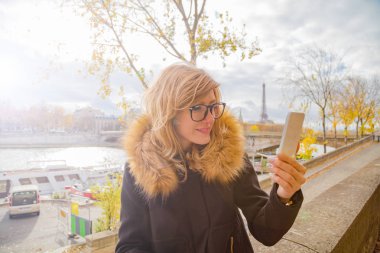 Paris geçmişi ve Eyfel kulesi olan cep telefonu kullanan bir kız..