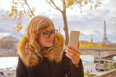 Paris geçmişi ve Eyfel kulesi olan cep telefonu kullanan bir kız..