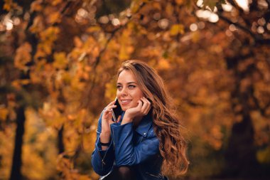 Sevimli kız Park sonbahar renkleri ile cep telefonu kullanarak.