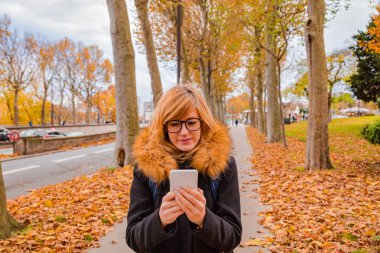 Kentsel sonbahar ortamda cep telefonu kullanan kız.