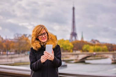 Paris geçmişi ve Eyfel kulesi olan cep telefonu kullanan bir kız..