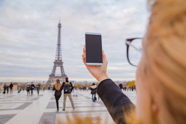 Paris geçmişi ve Eyfel kulesi olan cep telefonu kullanan bir kız..